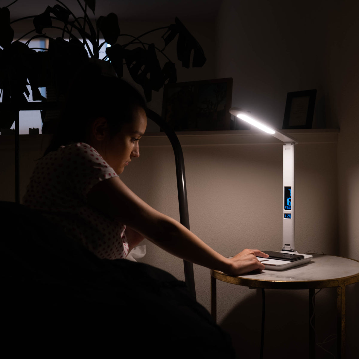 A woman turning a therapy lamp on next to her bed