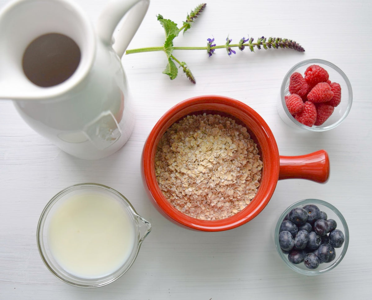 A bowl of oatmeal surrounded by fruits and a glass of milk