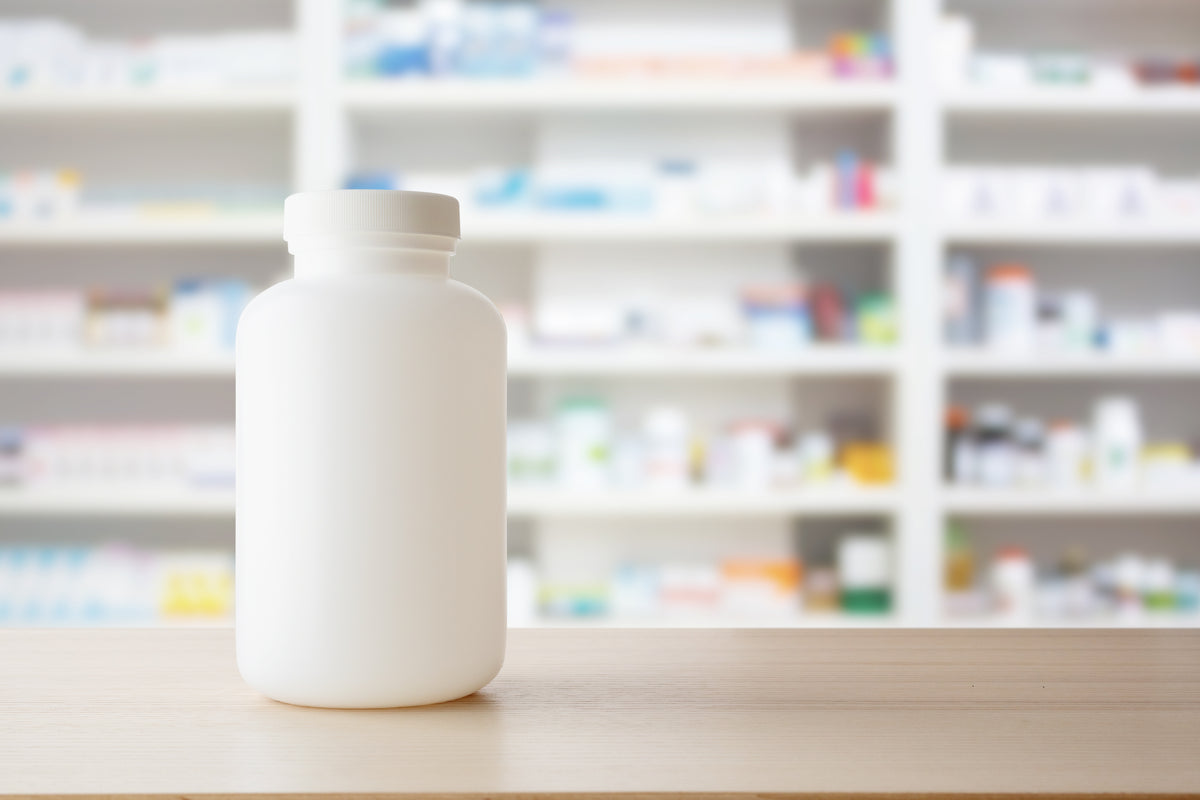 A white pill bottle in front of a shelf of medications