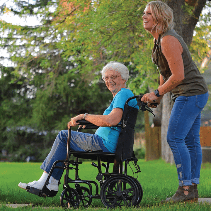 An elderly woman sitting in the ProBasics Aluminum Transport Chair being pushed by a caregiver