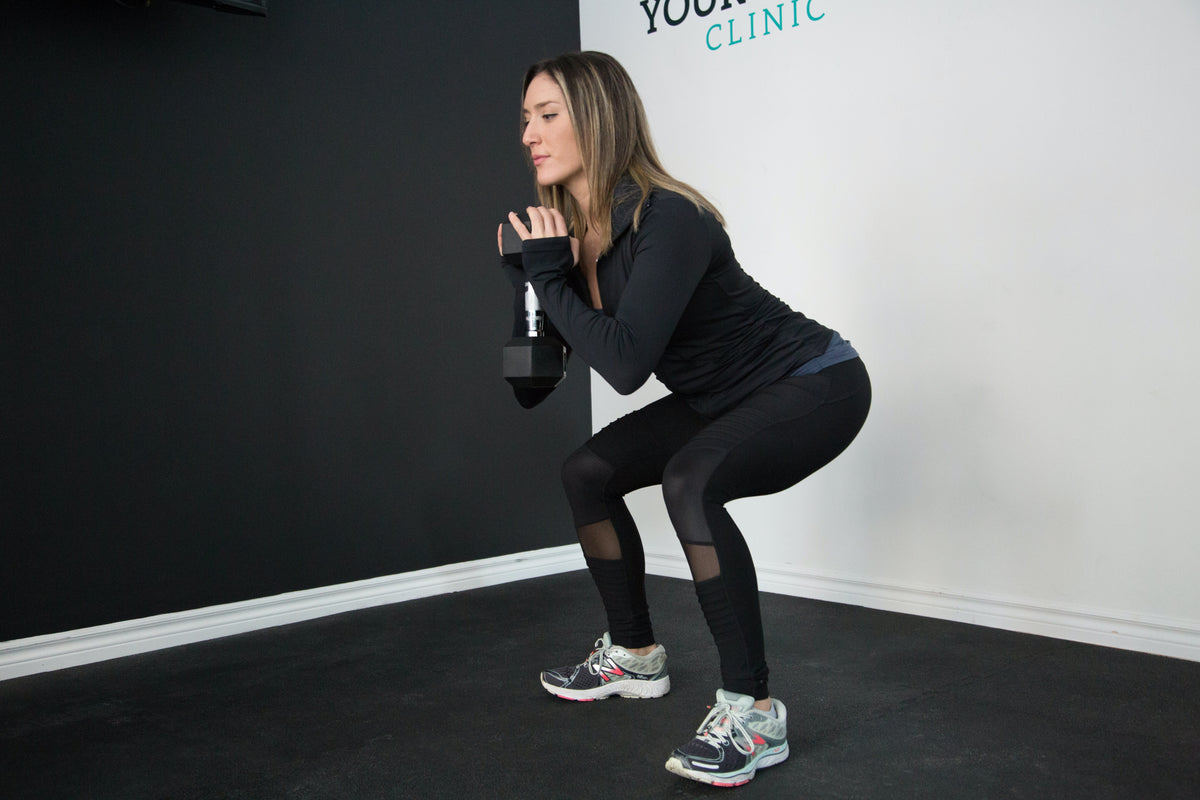 A woman doing a squat while holding a weight