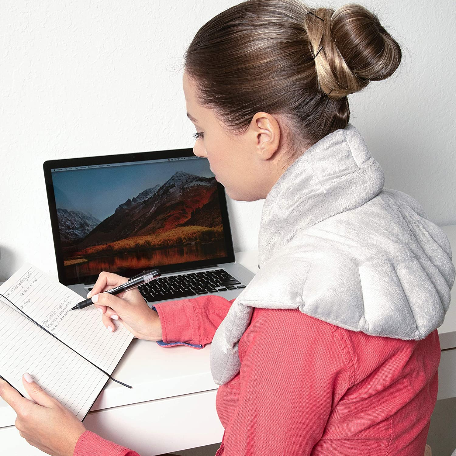 A woman writing in a journal with a hot/cold wrap on her shoulders