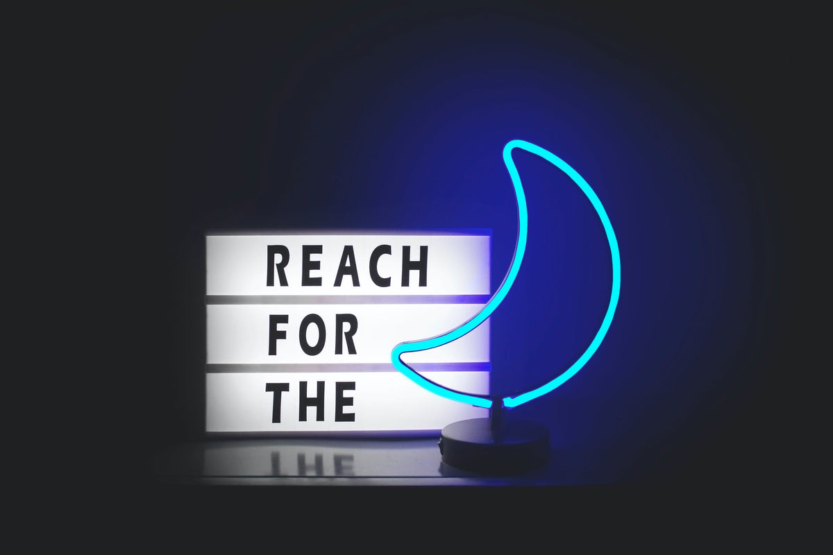 An illuminated moon and sign with text, “Reach for the”