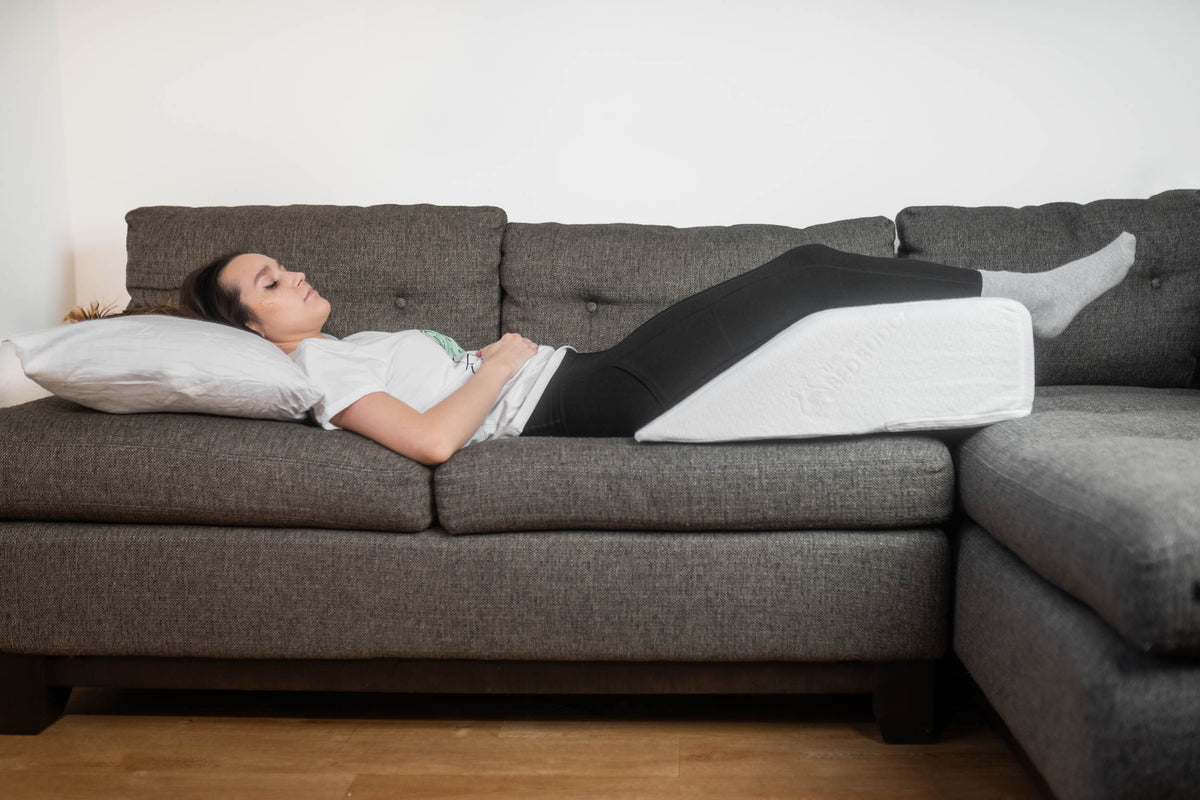 A woman sitting on a couch with a leg wedge pillow propping her knee up