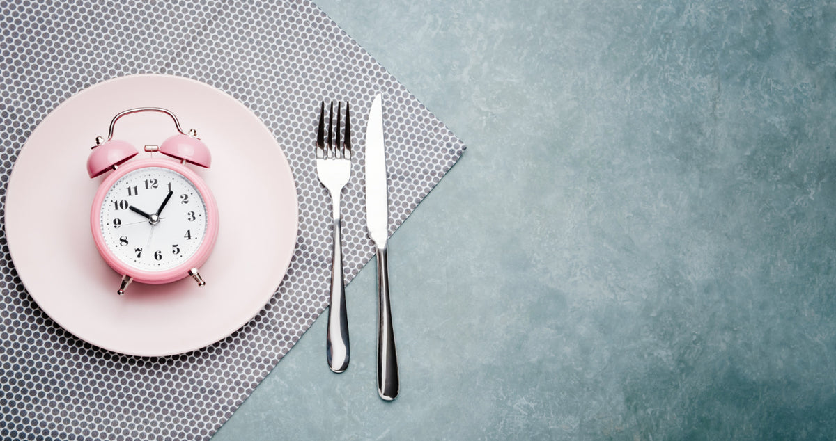 A clock on a plate next to a fork and knife