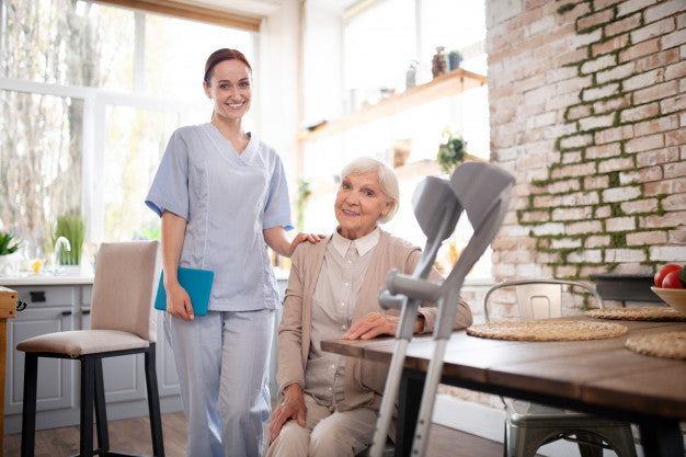 A caregiver standing next to a sitting elderly woman in front of crutches