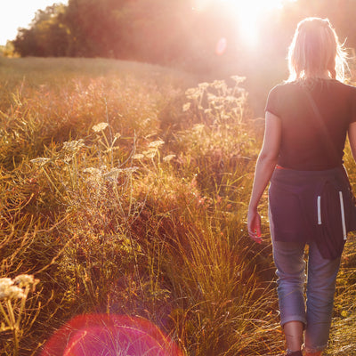 A woman walking in front of sun in a field of grass