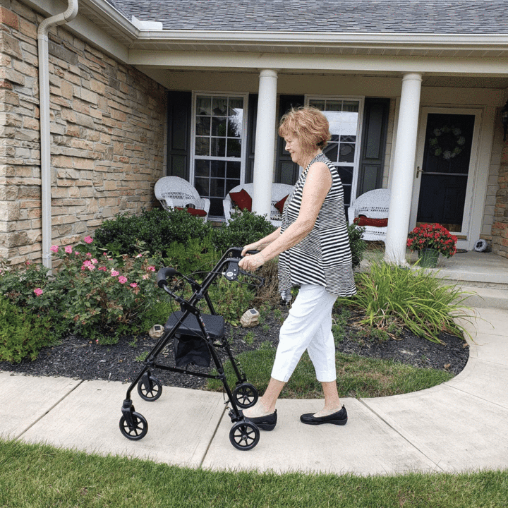A woman outside of her house on a sidewalk using the Carex Step ‘N Rest Rollator