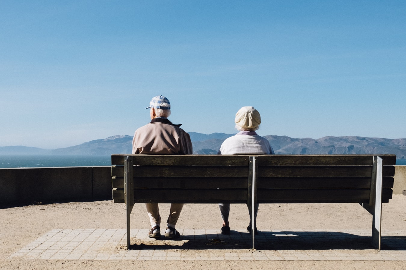 An elderly man and woman sitting on a bench overlooking  mountains