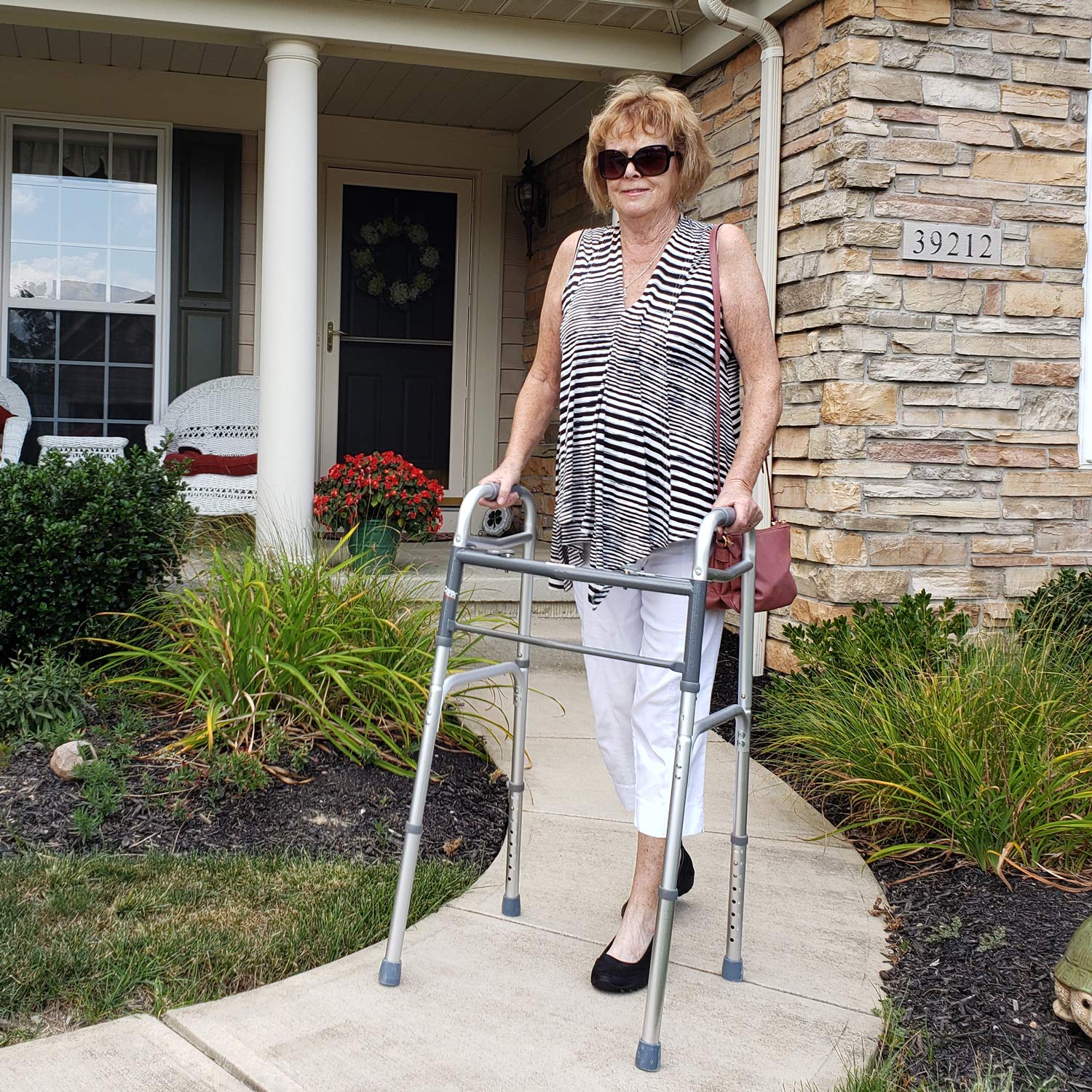 An elderly woman walking with a Walker outside her home