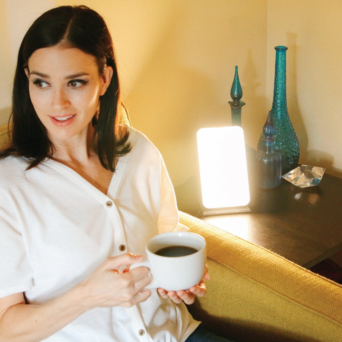 A woman with a cup of coffee next to a therapy lamp