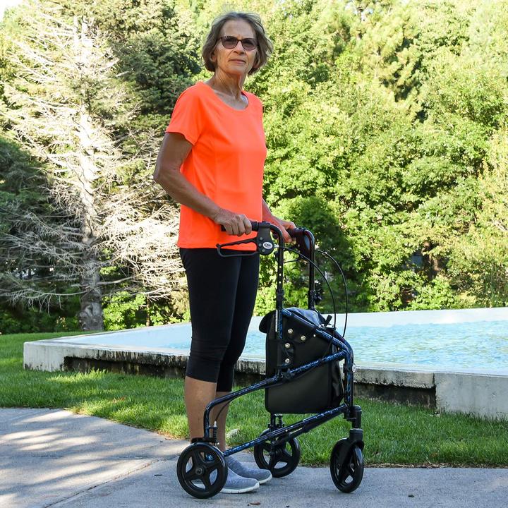 A woman walking on a sidewalk outside while using the Carex Trio Rollator