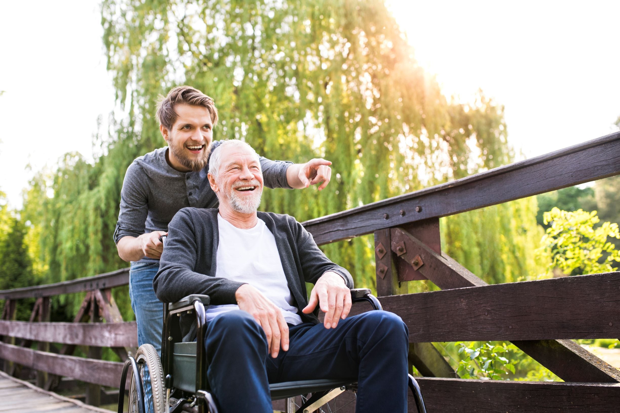 A smiling caregiver pushing an elderly man in a wheelchair while pointing