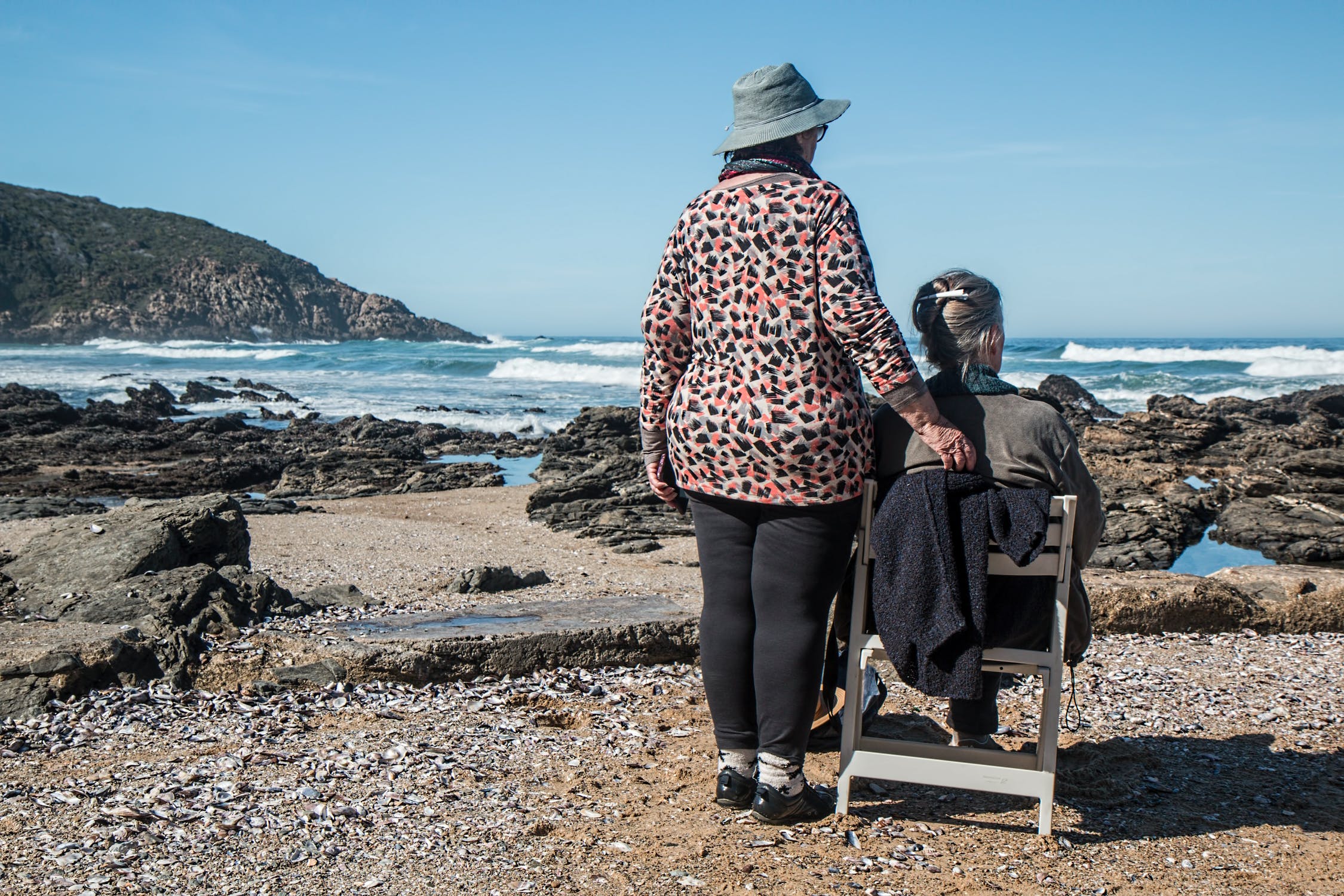 Two women at the beach with one sitting in a chair