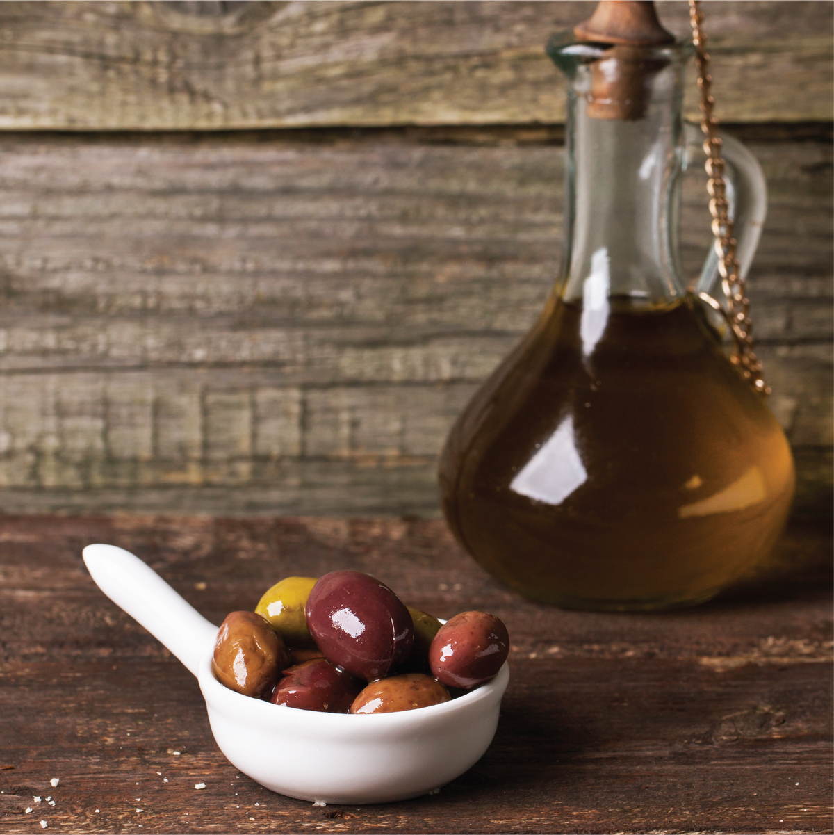 Olive in a dish in front of a bottle of olive oil