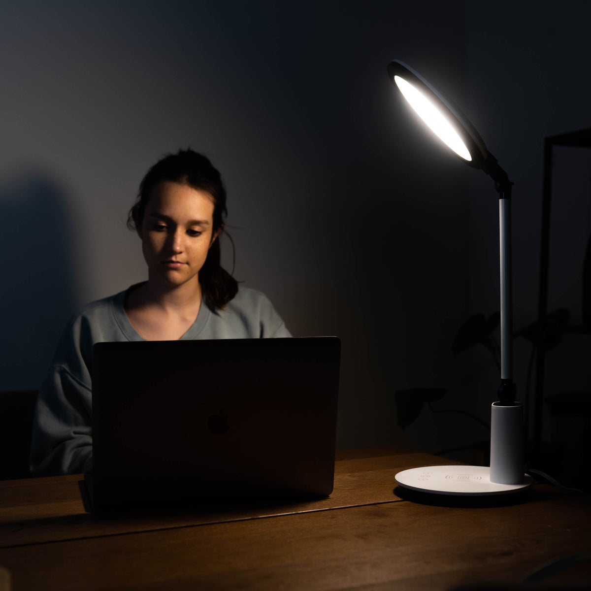A woman on her laptop next to a therapy lamp in a dark room