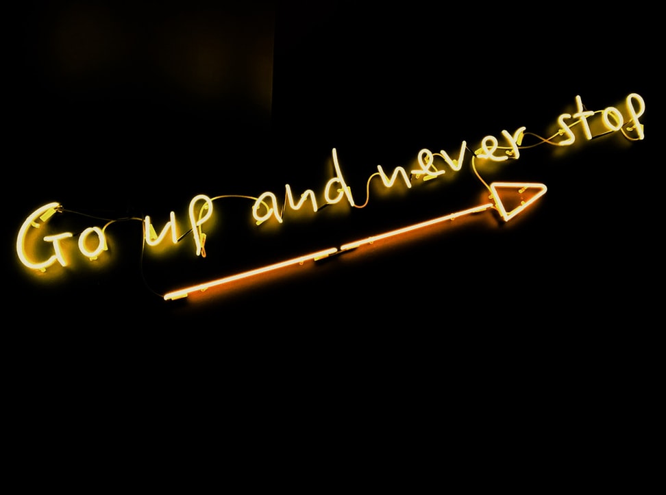 An illuminated sign that says “Go up and never stop” with an arrow below it