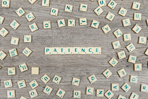 The word “patience” spelled out surrounded by various letters on a wood surface