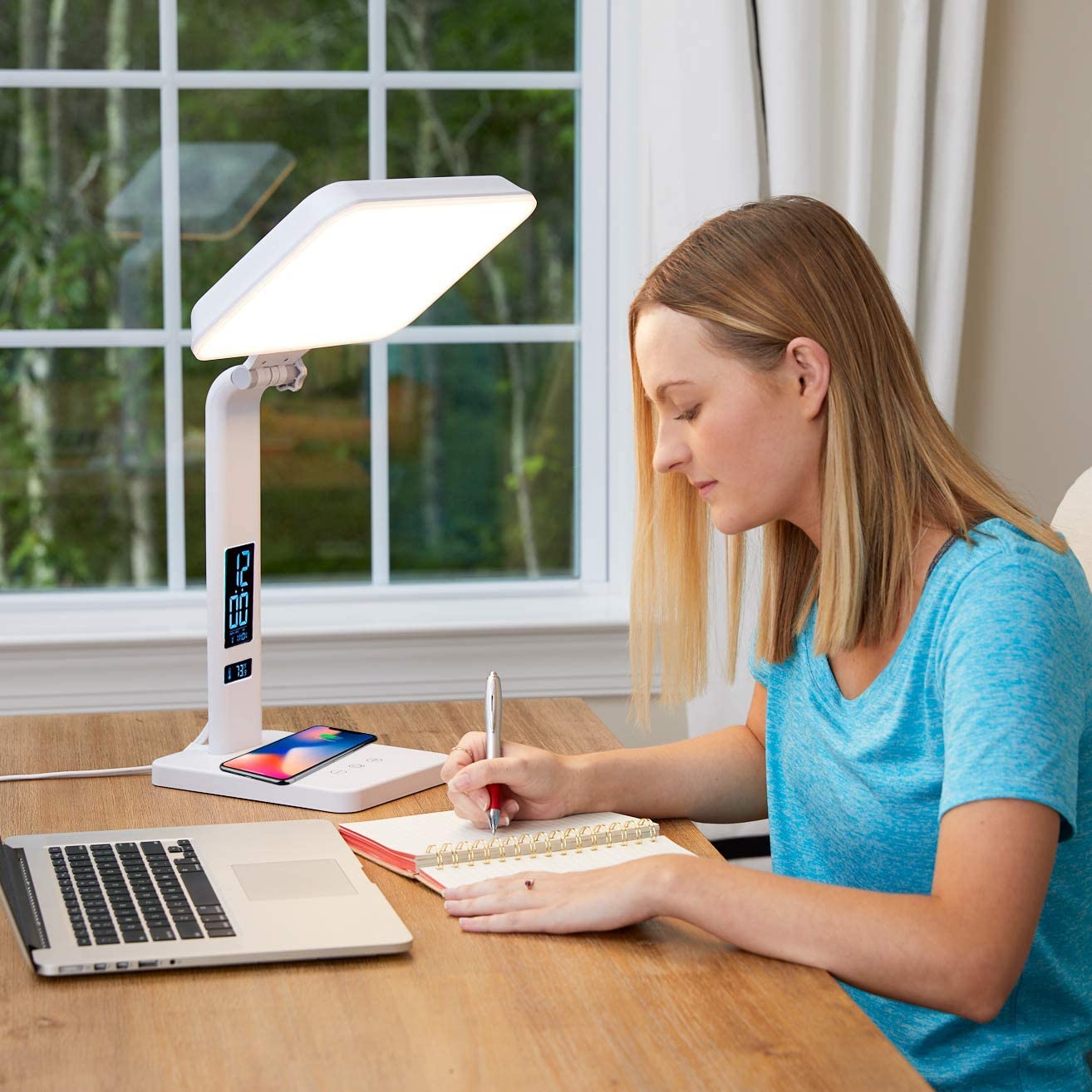 A woman sitting next to a light therapy lamp at her desk writing
