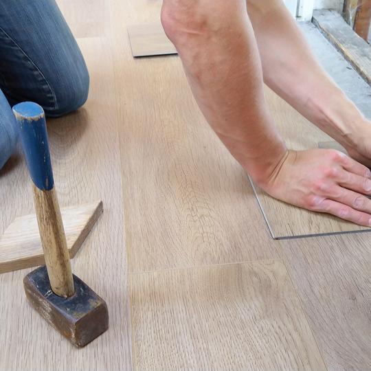 A close-up of a person installing wood flooring. 