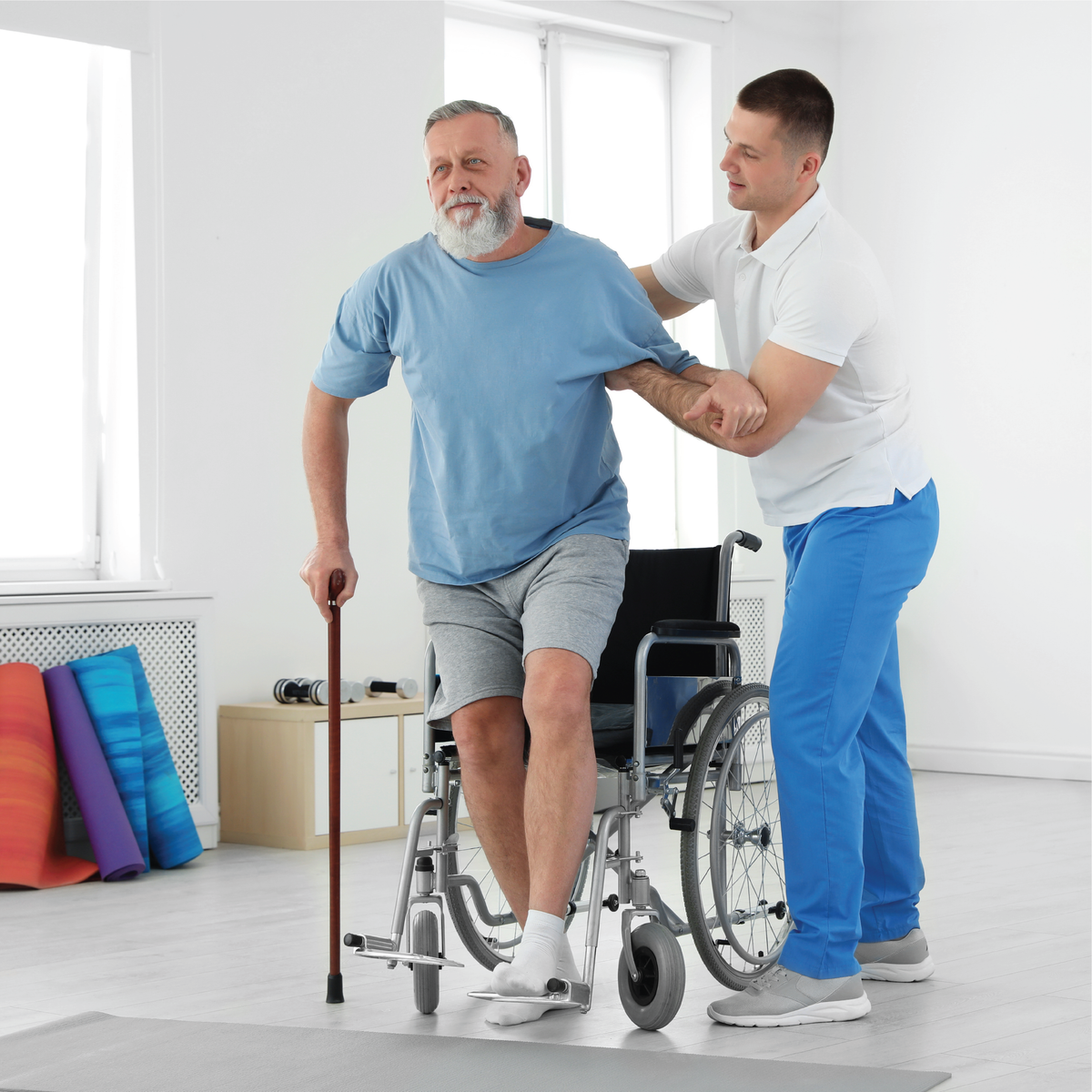 A man getting up from a wheelchair with the help of a physical therapist