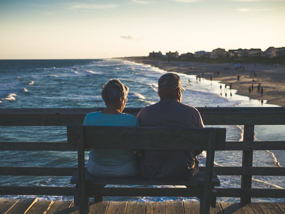 An elderly couple sitting on a bench in front of the beach