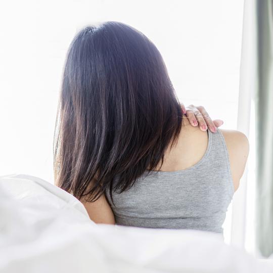 Woman in a gray tank top holding her neck, indicating pain or discomfort