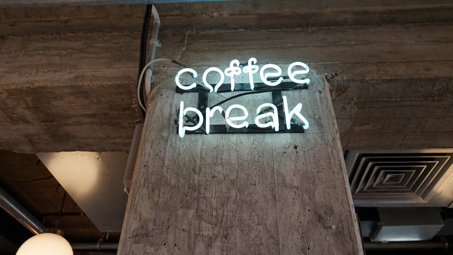 A neon sign on a concrete post that reads, “coffee break”
