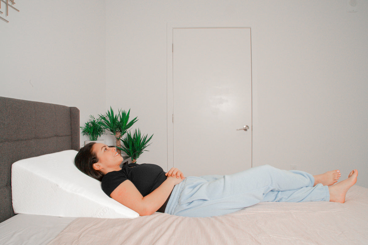 A woman laying in bed using a wedge pillow on her back