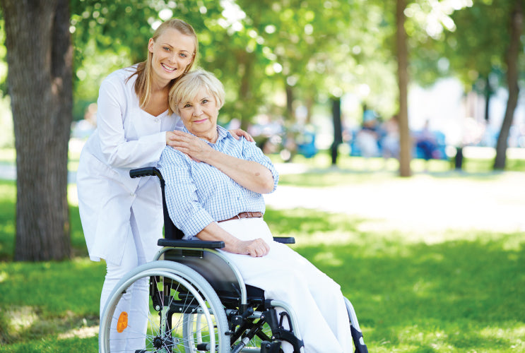 A caregiver hugging an elderly woman in a wheelchair in a park
