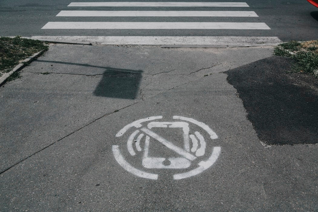 A cross walk with a spray painted no phone icon