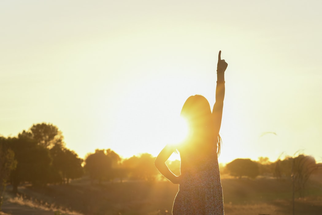 A woman with her hand up in front of the sky