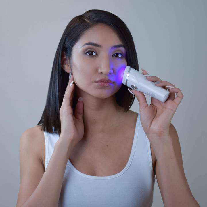 A woman using the reVive Light Therapy® Spot over her fact on a grey background