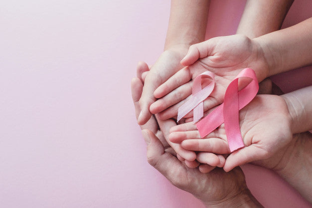 Two pairs of hands holding a pink cancer ribbon