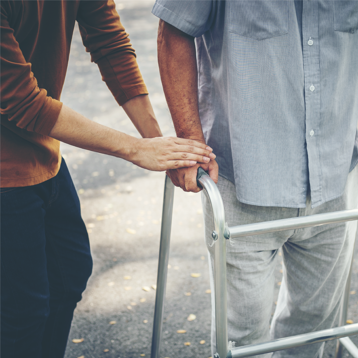 A woman holding an elderly man’s hand while using a walker