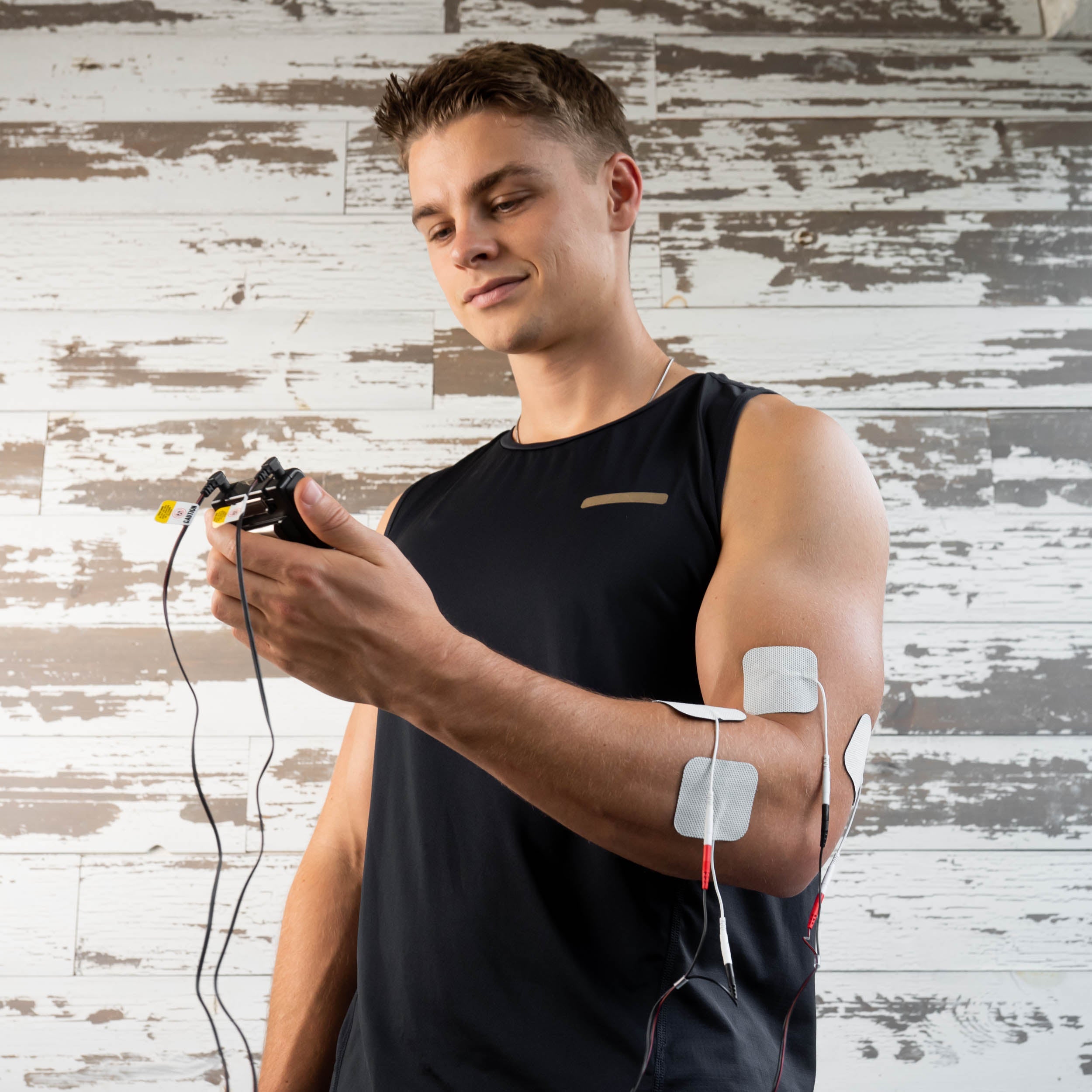 A man holding a TENS unit with electrodes on his elbow
