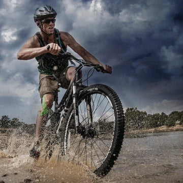 A man riding a bike through mud with kinesiology tap on his knee