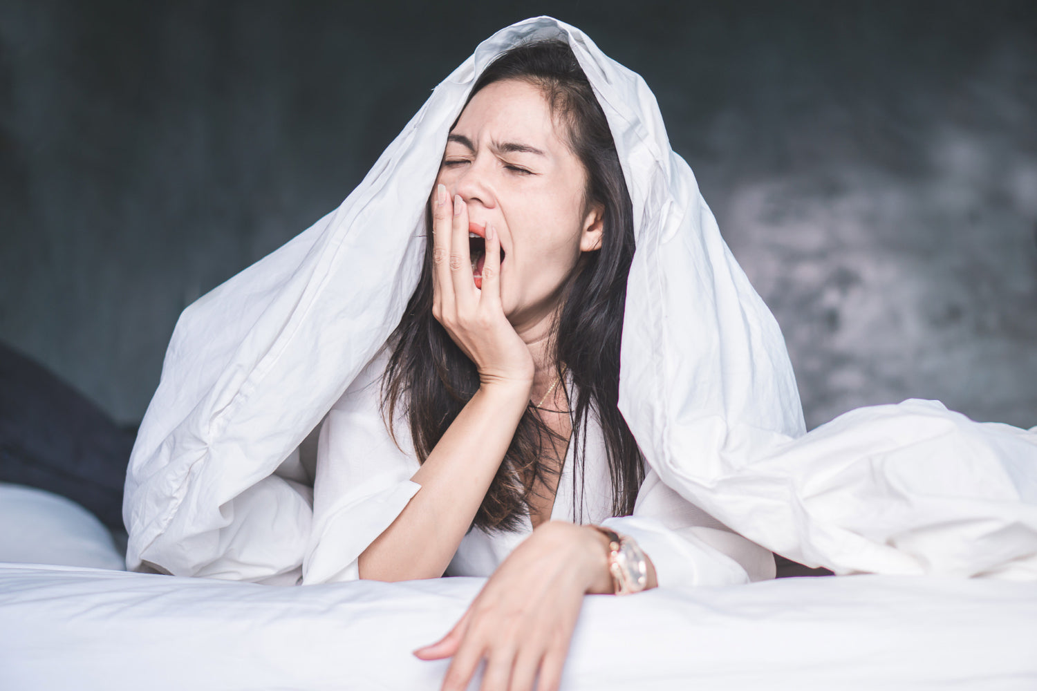 A woman yawning while laying under a blanket