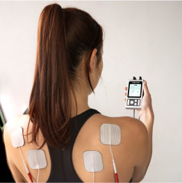 A back view of a woman holding the TENS 7000 Rechargeable TENS unit with electrodes on her back.