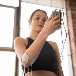 A woman holding the TENS 7000 Rechargeable TENS Unit with electrodes on her elbow