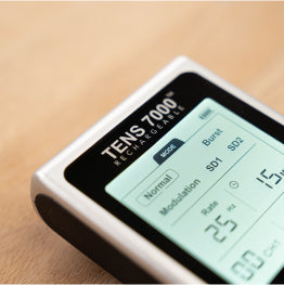 A close up of the TENS 7000 Rechargeable TENS Unit’s backlit screen on a wood surface 