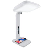 A white therapy lamp with a squar head and cell phone charging on it.