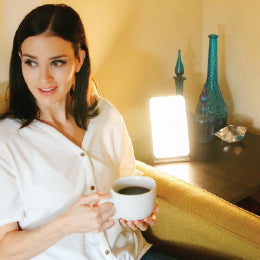 A woman enjoying coffee basking next to the TheraLite therapy lamp