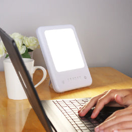 The TheraLite Glow next to a laptop with someone typing