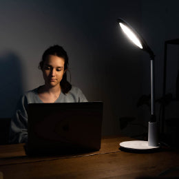 A woman on her laptop basking under the TheraLite Radiance therapy lamp