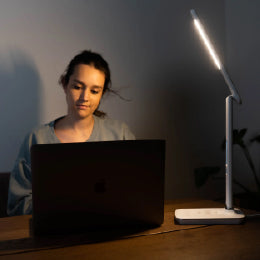 A woman on her laptop basking under the TheraLite Radiance therapy lamp