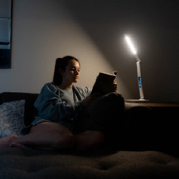 A woman reading a book basking under the TheraLite Radiance therapy lamp