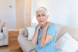 An elderly woman holding her shoulders with chronic pain