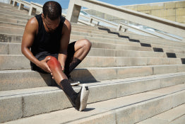 A male athlete sitting on bleachers holding his knee in pain