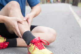 A man experiencing shin splints while sitting on concrete